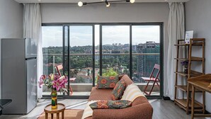 A modern living room with a large window, a sofa, a coffee table, and a refrigerator.
