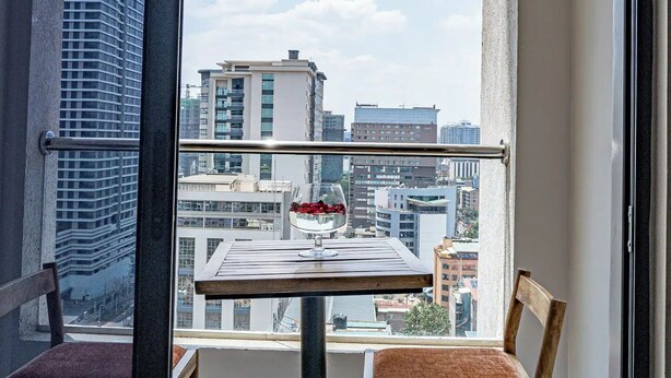 A balcony with a table and chairs, a view of the cityscape, and a clear sky. - Elite - 1 bedroom - pool & Gym

 (Nairobi)