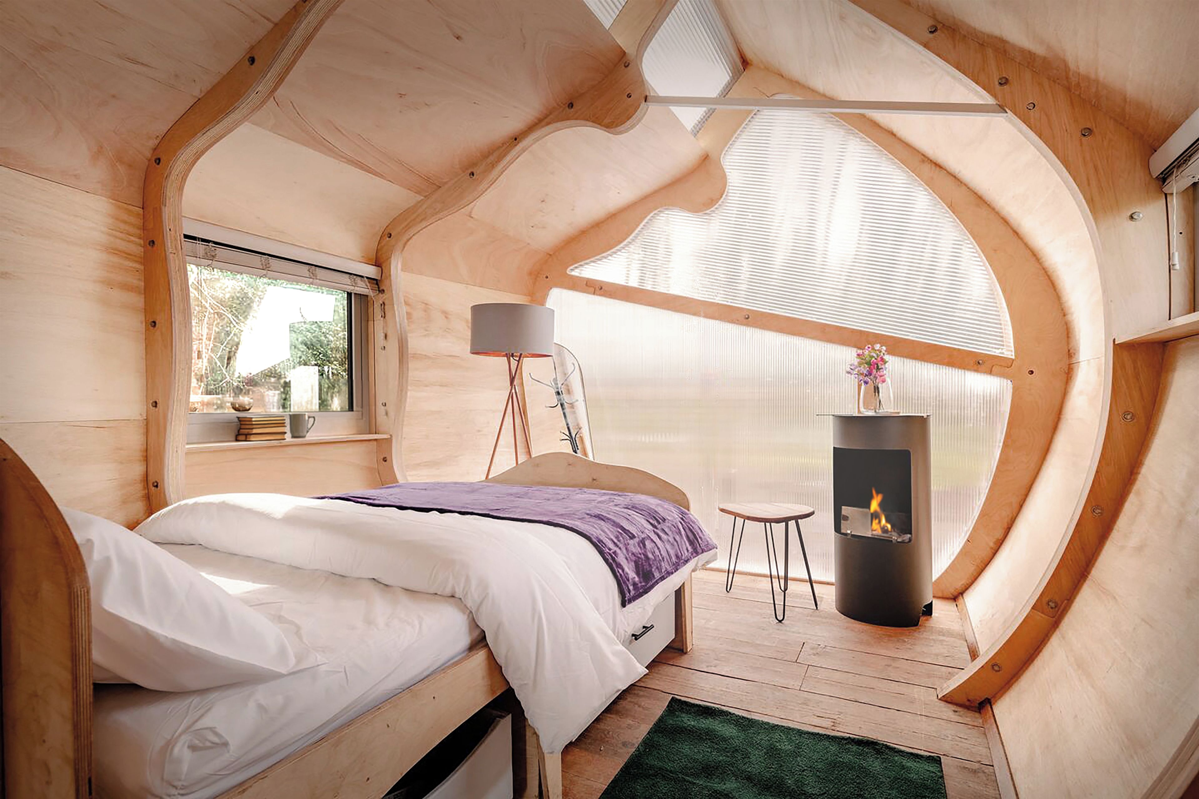 A cozy bedroom with a bed, a window, a lamp, a small table, and a fireplace.