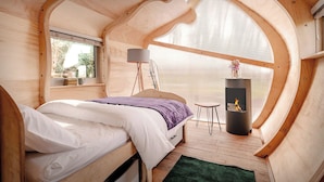 Un dormitorio acogedor con cama, ventana, lámpara, una mesita y chimenea.