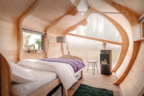 Un dormitorio acogedor con cama, ventana, lámpara, una mesita y chimenea.