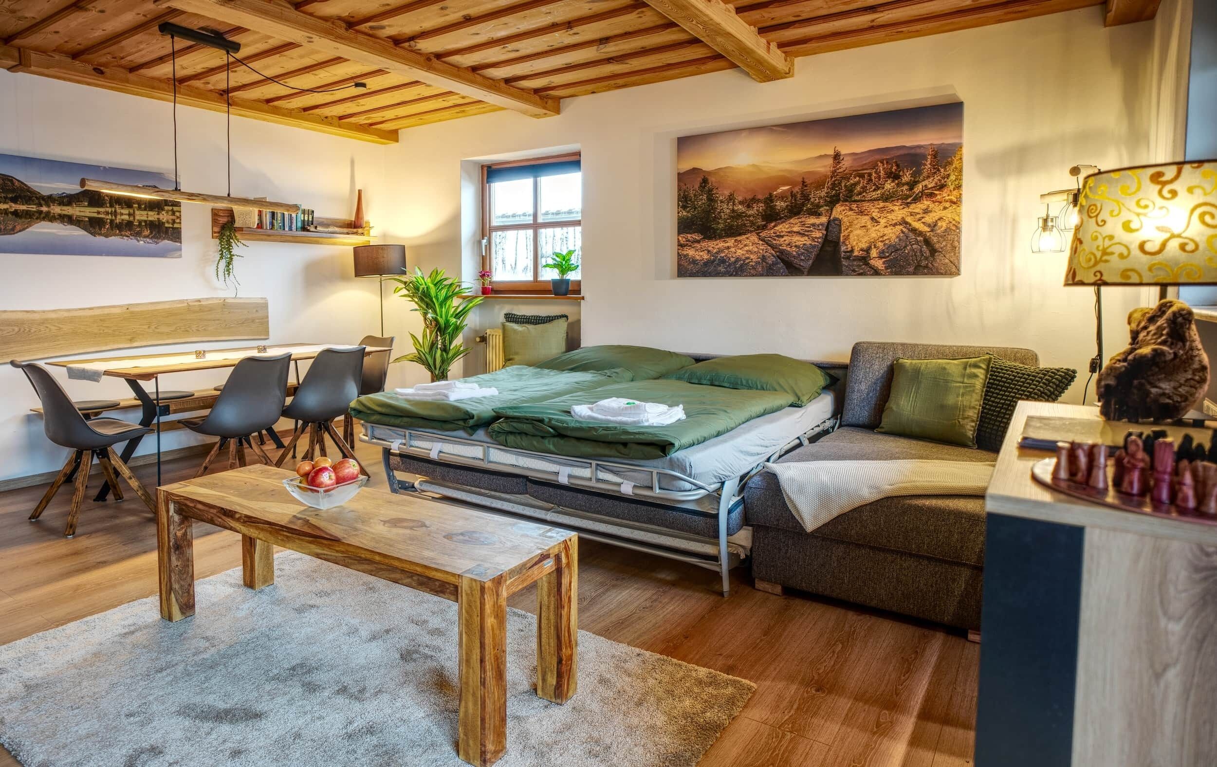 A cozy room with a bed, a desk, and a couch. There is a window with a view of trees and mountains.