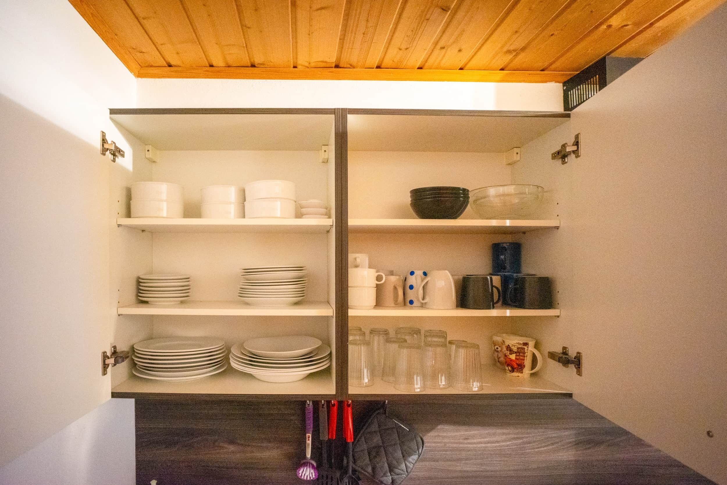 A kitchen with white cabinets, shelves with dishes, cups, and a kettle.