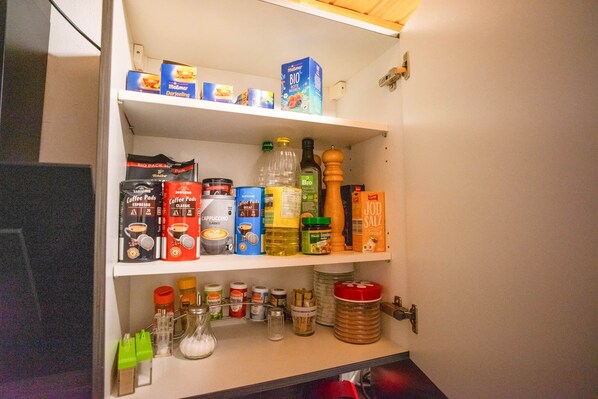 A kitchen pantry with shelves stocked with coffee pods, jars, and condiments.