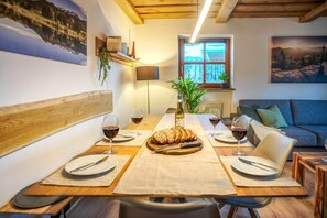 A dining area with a wooden table set for four, two wine glasses, a loaf of bread, and a bottle of wine.