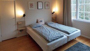 Un dormitorio con dos camas, una ventana que da a árboles y tres cuadros en la pared.