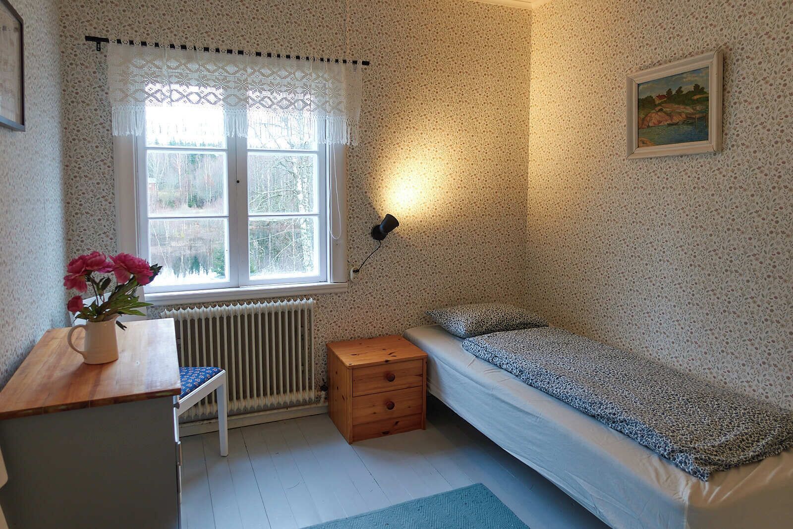 Une chambre à coucher avec un lit, un bureau, une chaise, un radiateur et une fenêtre ornée de rideaux en dentelle.
