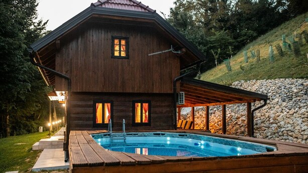 Une cabane en bois avec une piscine, entourée d’un mur de pierre et dotée d’un patio couvert.