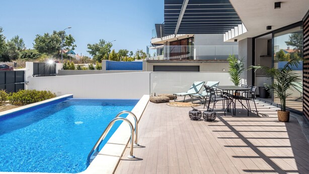 Zona de piscina en la azotea con piscina azul cristalina, sillas de descanso, una mesa y plantas en macetas.