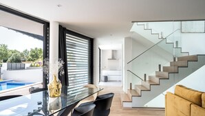 Una sala de estar moderna con una mesa de comedor de vidrio, sillas negras, un sofá amarillo y una escalera con barandilla de cristal.