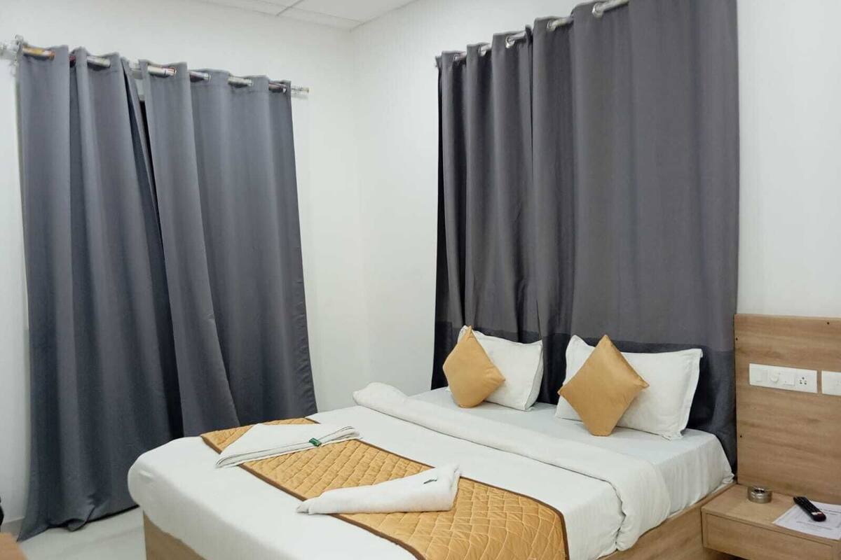 A hotel room with a bed, curtains, a bedside table, and a nightstand.