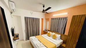 A hotel room with a bed, a ceiling fan, a TV, and curtains. - Hotel Habitat Inn - Pune (Pune)
