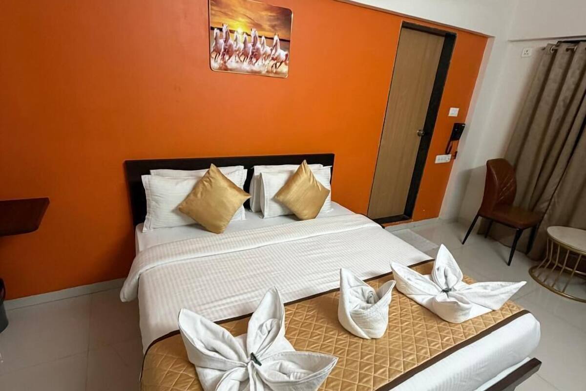 A hotel room with a bed, a ceiling fan, an orange wall, and a door.