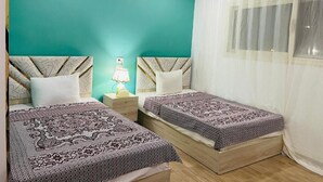 A room with two beds, a teal accent wall, a window with sheer curtains, and a bedside lamp. - Farida Pyramids Boutique Hotel (Giza)