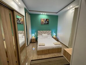 Une chambre moderne avec un grand lit, deux tables de chevet avec des lampes, une tête de lit ornée d’un motif géométrique et un tableau accroché au mur.