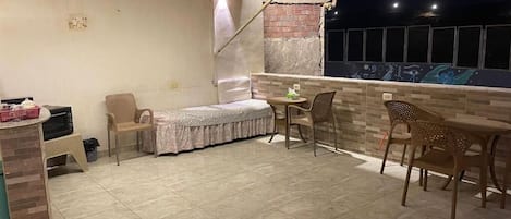 A rooftop terrace with a bed, chairs, a table, and a brick wall.