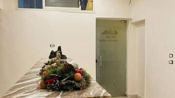 Un mostrador de recepción de mármol con un arreglo decorativo de laurel, una puerta con un letrero y un suelo de baldosas.