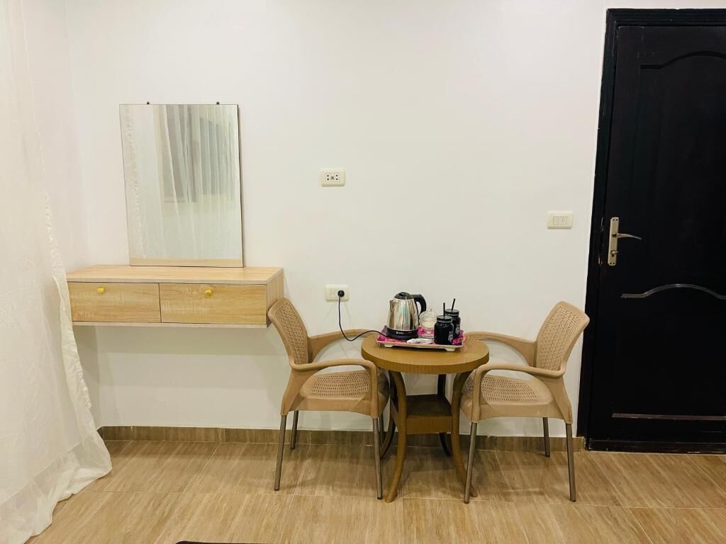 Una habitación pequeña con un escritorio de madera, dos sillas, una mesa redonda con una tetera y una taza, y una puerta negra.