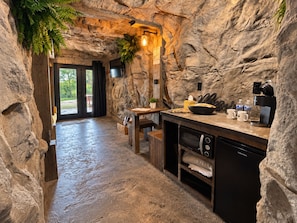 A rustic kitchen with a stone wall, wooden counter, and a view of the outdoors.