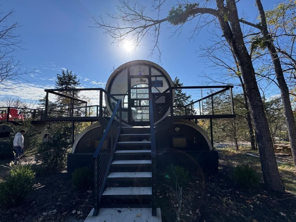 A circular structure with a glass entrance, surrounded by stairs and metal railings, set in a wooded area.