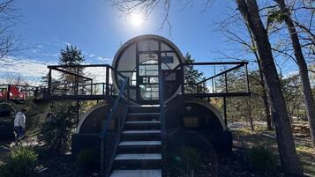 A circular structure with a glass entrance, surrounded by stairs and metal railings, set in a wooded area.