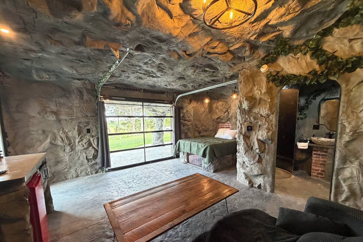 A rustic stone interior with a wooden bench, a bed, and a stone sink.