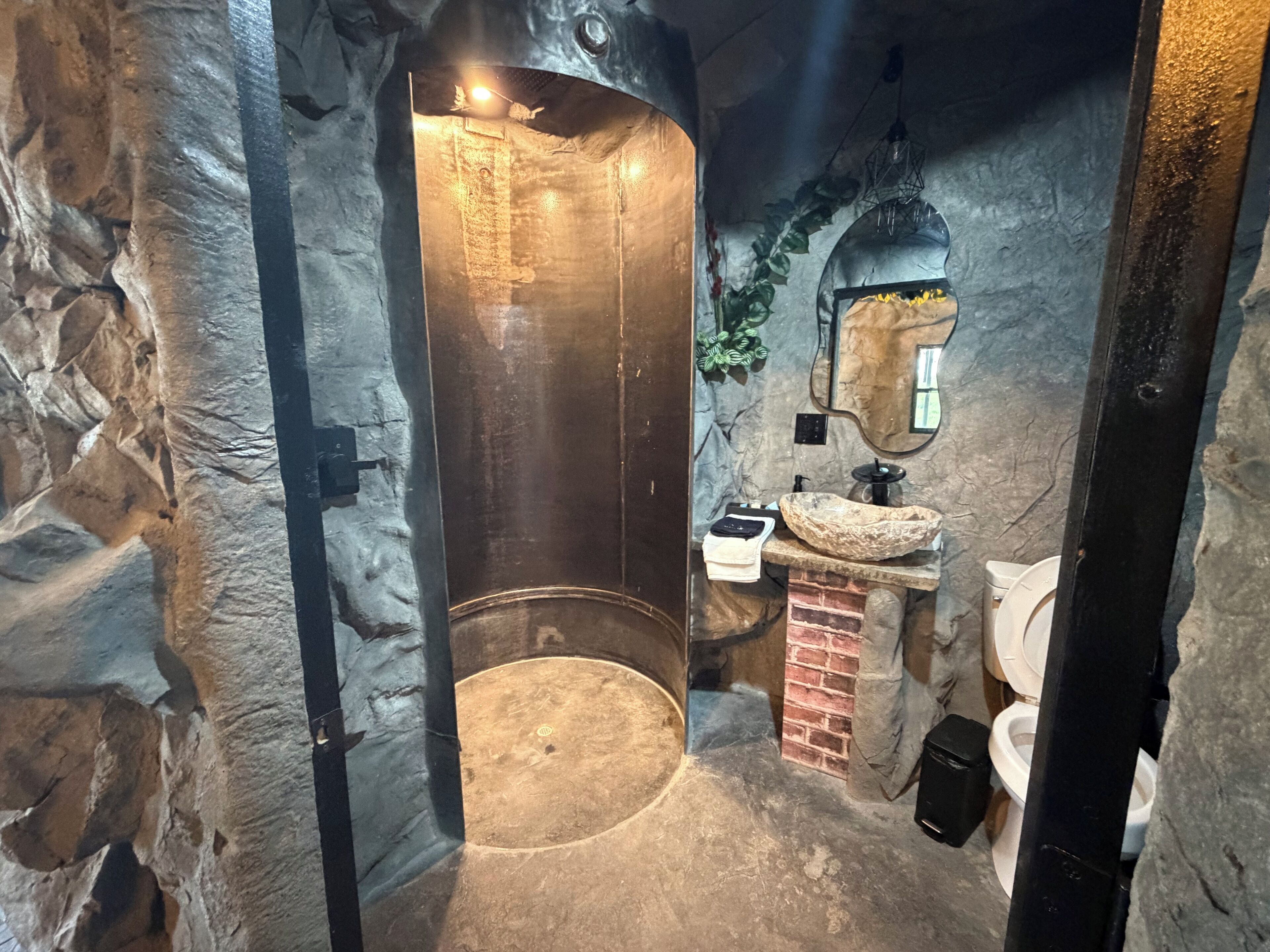 Een badkamer met stenen muren, een rond wastafel, een spiegel en een toilet.