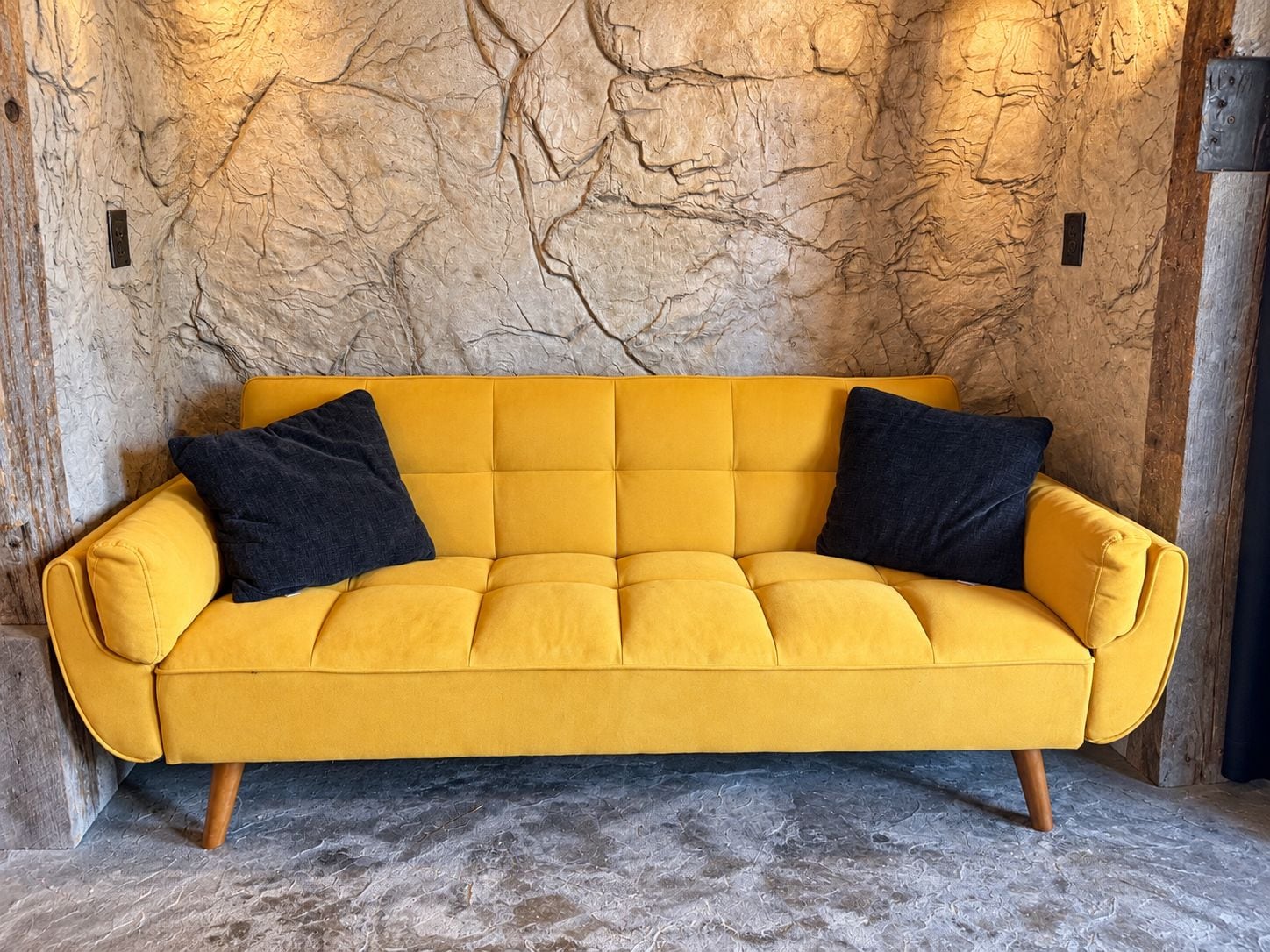 Un sofá amarillo con patas de madera frente a una pared con textura.