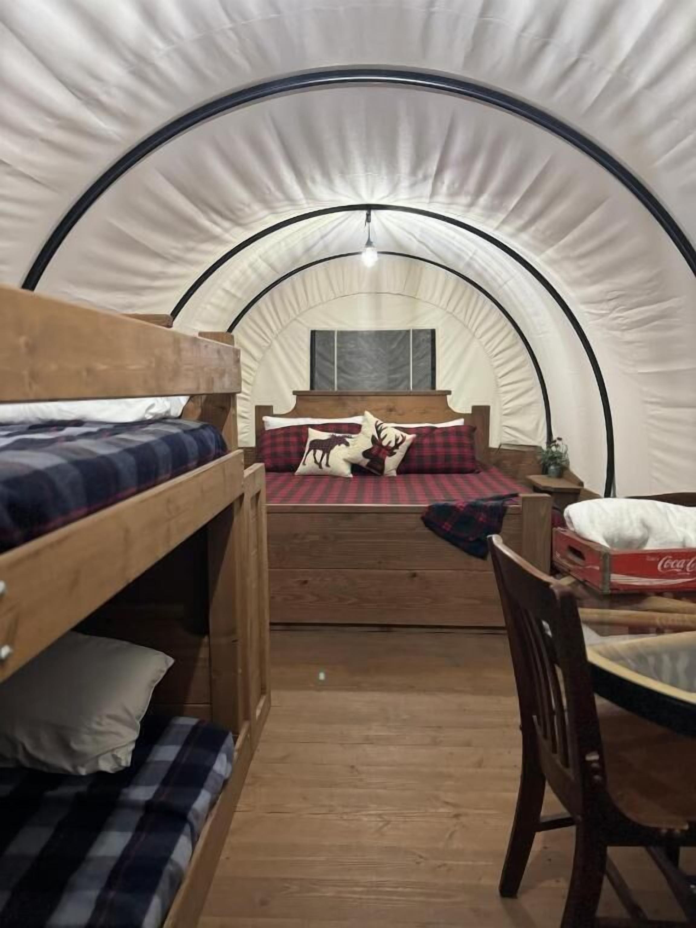 Ein Zeltraum mit Etagenbetten, einem Holztisch und einem Bett mit karierter Decke.