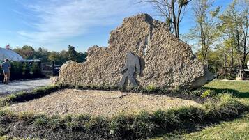 Un'imponente formazione rocciosa con una figura scolpita, circondata da erba e alberi.