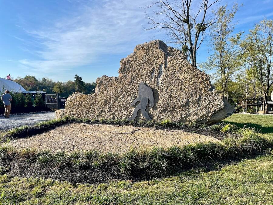Un'imponente formazione rocciosa con una figura scolpita, circondata da erba e alberi.