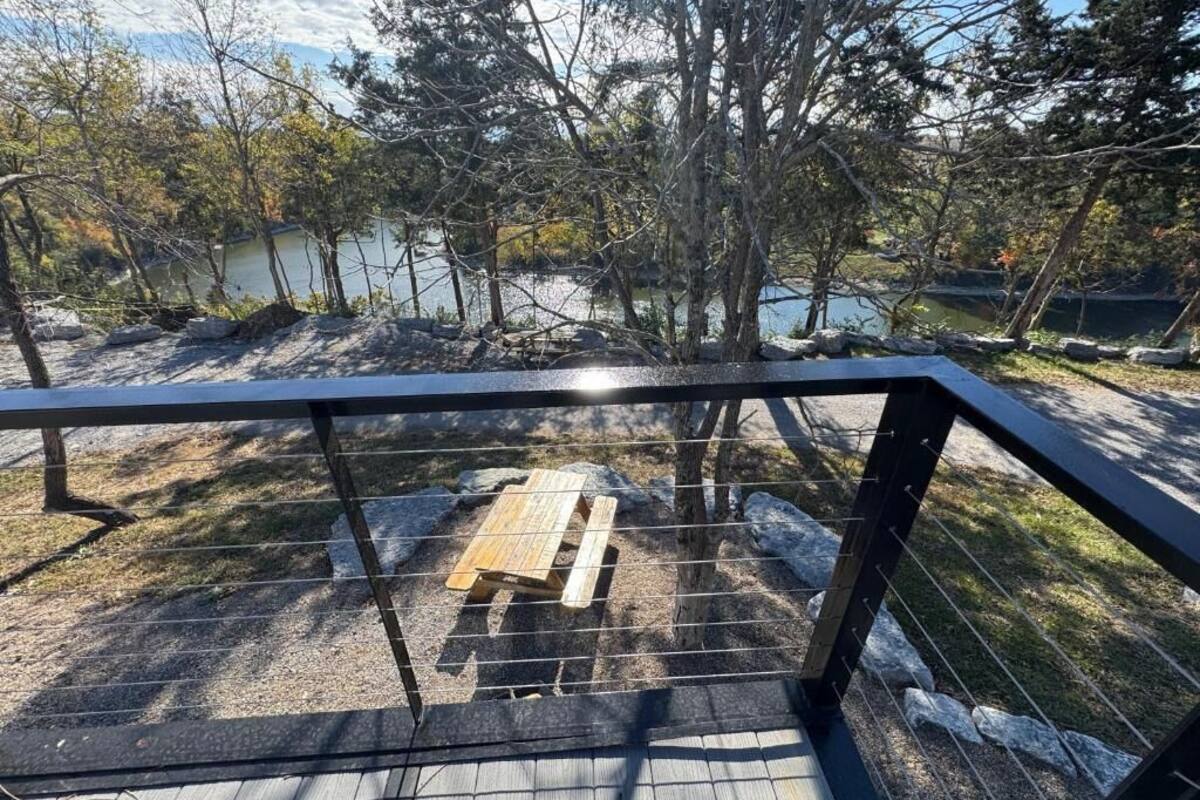 A wooden deck with a metal railing overlooking a lake, surrounded by trees.