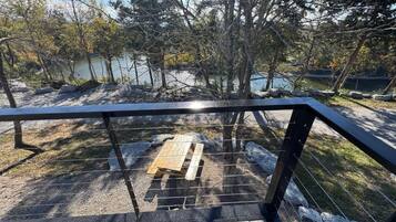 Una terraza de madera con barandilla de metal que da a un lago, rodeado de árboles.