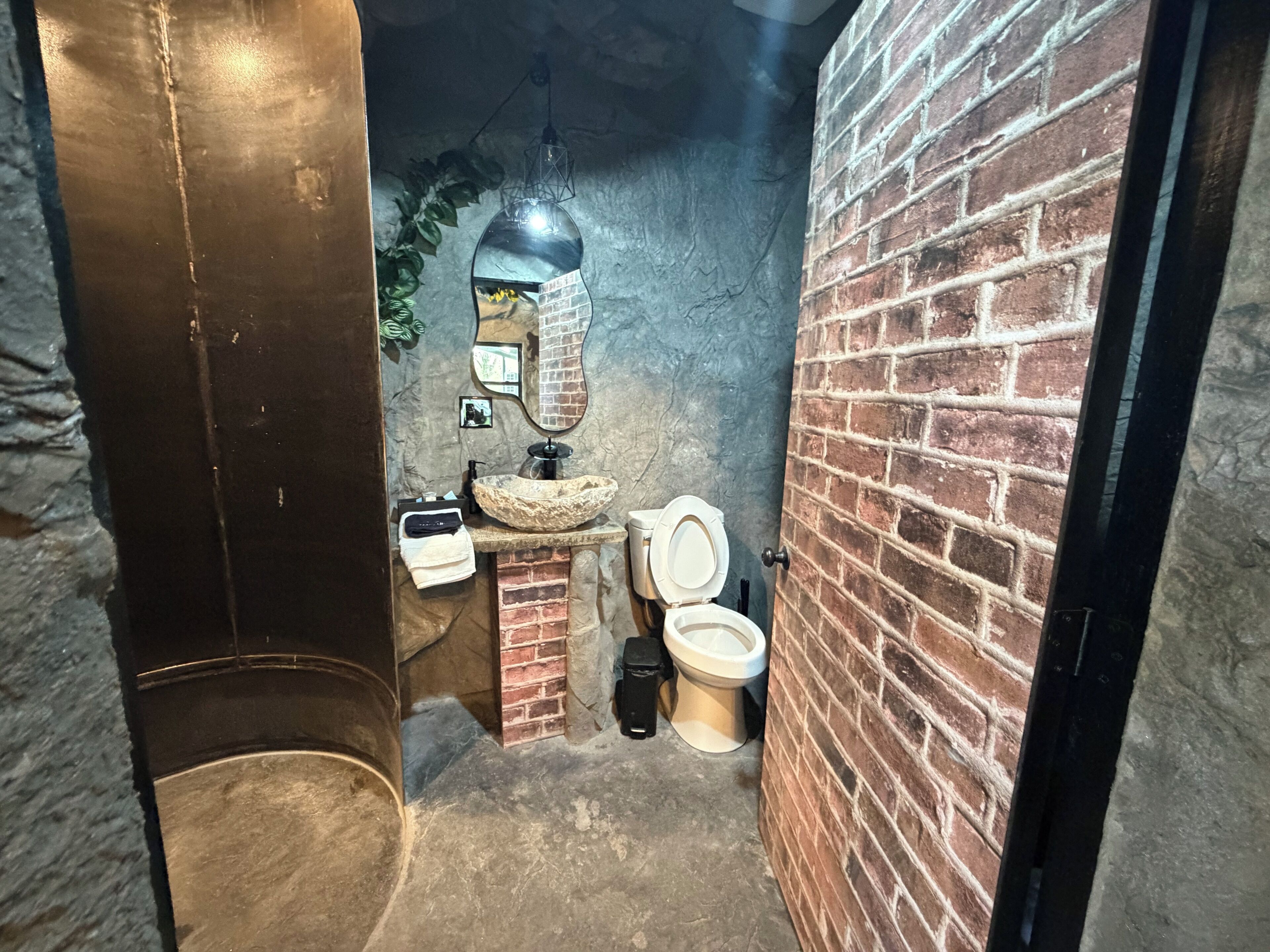 Une salle de bain avec un lavabo en pierre, deux toilettes, un miroir et un luminaire suspendu.