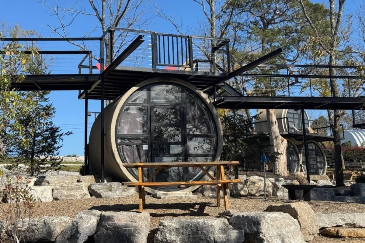 A large cylindrical structure with a metal framework, surrounded by rocks and trees.