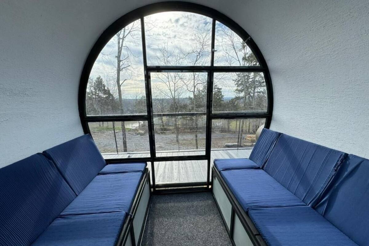 A room with a large arched window, two blue cushioned benches, and a view of trees and a body of water.