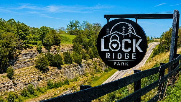 A sign for Lock Ridge Park with a scenic view of a winding road and rocky terrain.