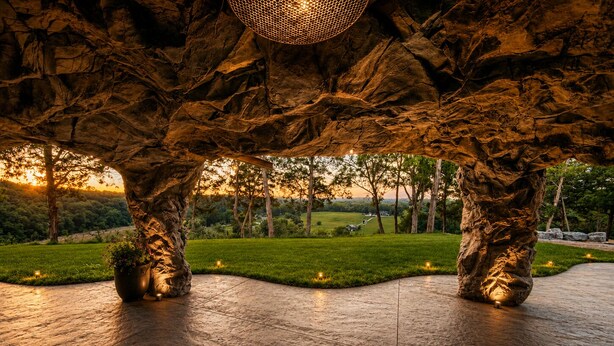 An indoor space with a stone floor, large rock-like structures, and a view of a grassy landscape at sunset. - LockRidge Park (Lancaster)