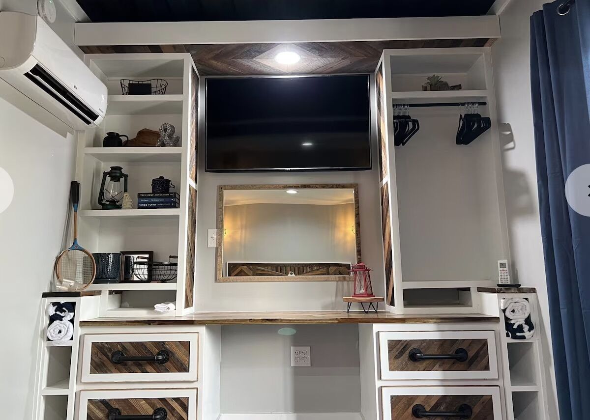 A room with a TV mounted above a mirror, shelves with various items, and storage drawers.