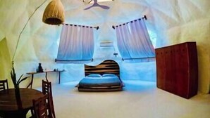 An igloo-style room with a bed, two windows with curtains, a table with chairs, and a hanging light fixture. - Casa Leon Global, 3 Domes In Mayan Jungle (Cancún)
