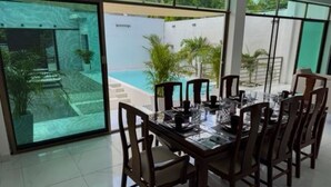 Ein Essbereich mit großem Tisch und Stühlen, große Fenster mit Blick auf einen Pool und Grünflächen.