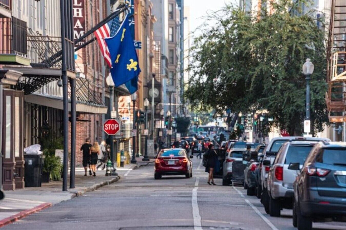 A street lined with parked cars, a stop sign, and a flagpole with flags.