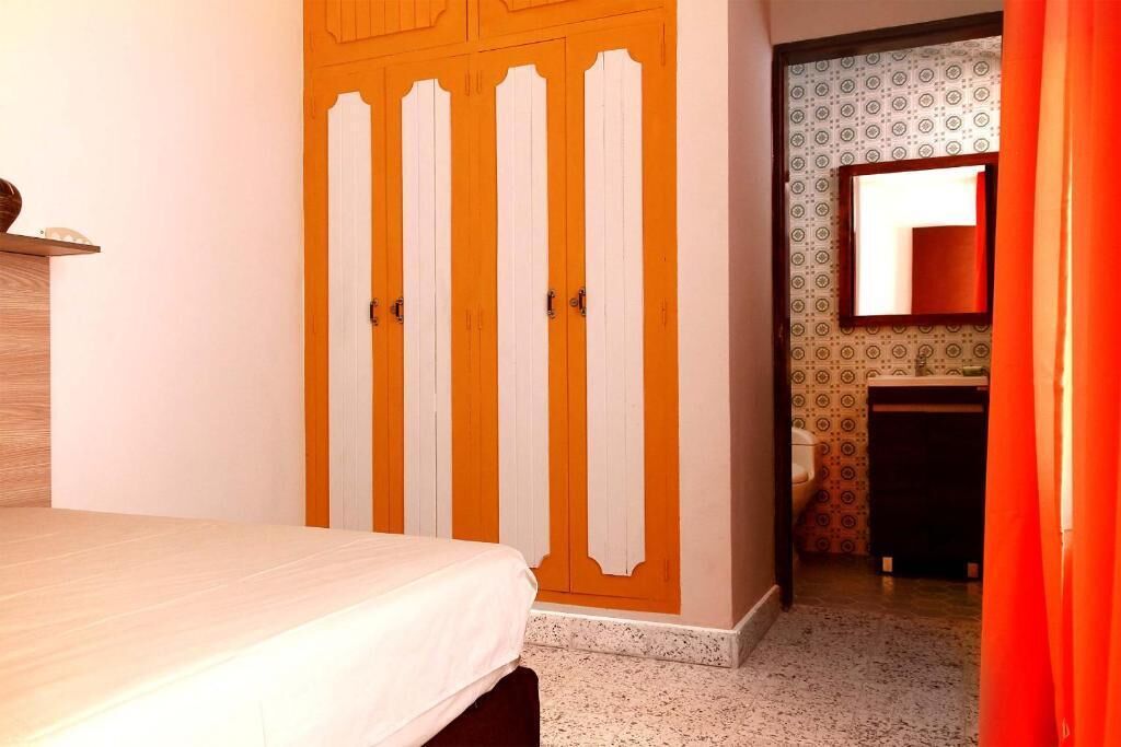 Un dormitorio con cama, armario y baño visible a través de una puerta abierta.