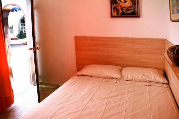 Un dormitorio con cabecera de madera, una cama con ropa de cama color beige y una puerta que da a un espacio exterior.