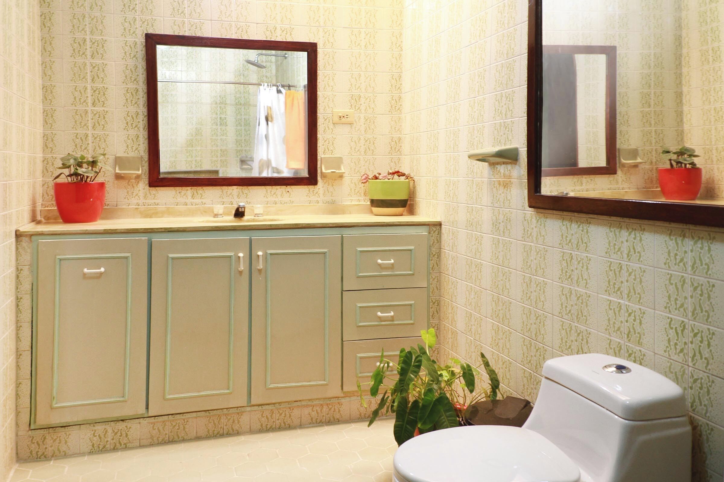 A bathroom with a toilet, a sink with a mirror above it, and two potted plants on the counter.