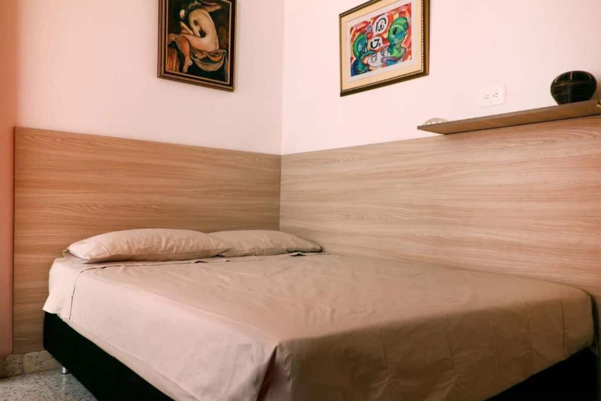 Quarto com cabeceira de madeira, cama com roupa de cama bege e duas obras de arte emolduradas na parede.