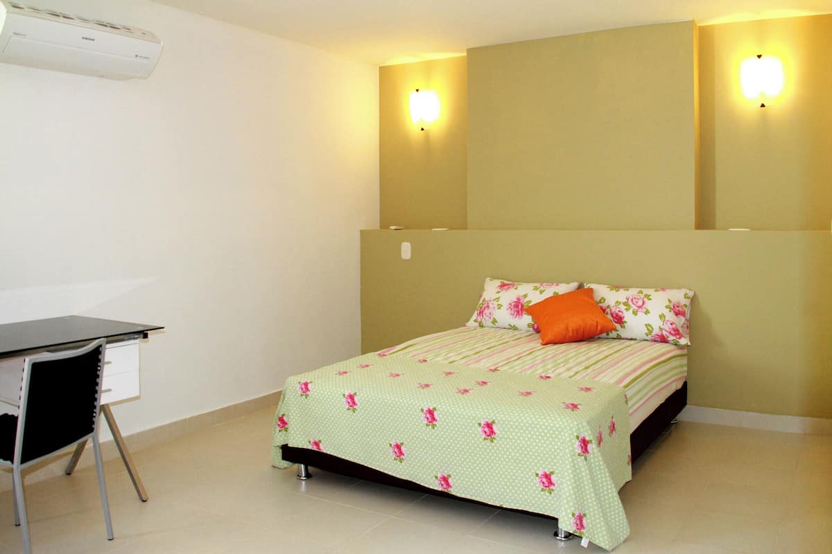 Quarto com uma cama, escrivaninha e ar condicionado.