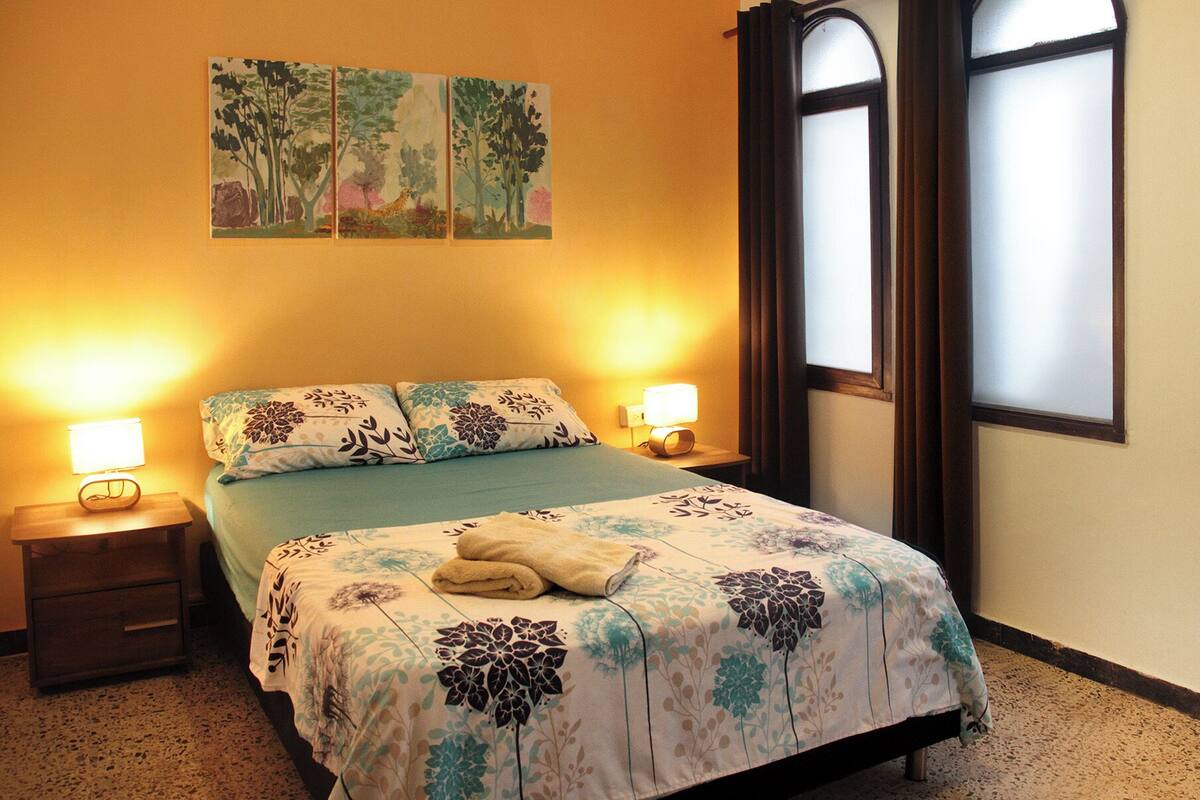 Quarto com cama, duas luminárias de cabeceira, mesa de cabeceira e janela com vidro jateado.