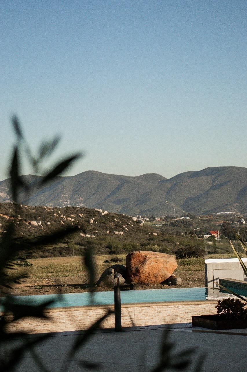 Un espace piscine agrémenté d’un grand rocher, avec une chaîne de montagnes en arrière-plan et un ciel dégagé.