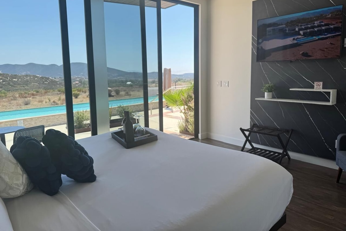Quarto com uma cama grande, televisão na parede e vista para uma piscina e montanhas.